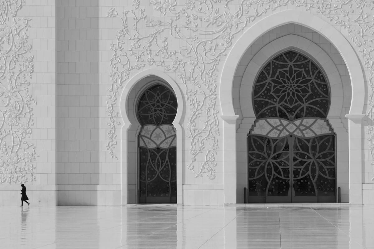 Black and white photo of a woman walking in front of the Sheikh Zayed Grand Mosque in Abu Dhabi