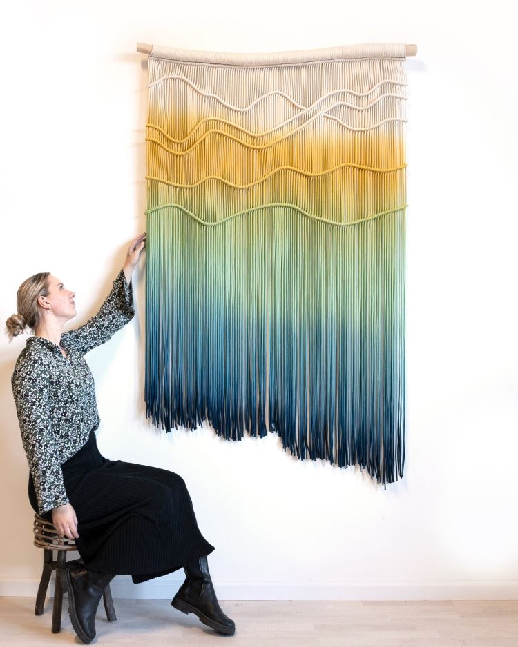 Rianne Aarts Standing In Front Of Wall Hanging Made Of Fiber Featuring A Yellow To Blue Gradient