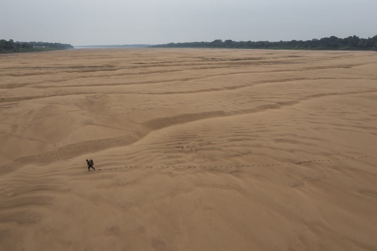 A fisherman walks across the dry bed of a branch of the Amazon River, near the Porto Praia Indigenous community. Tefé, 